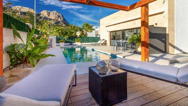 A modern outdoor pool area with a wooden pergola, lounge chairs, and a dining area.
