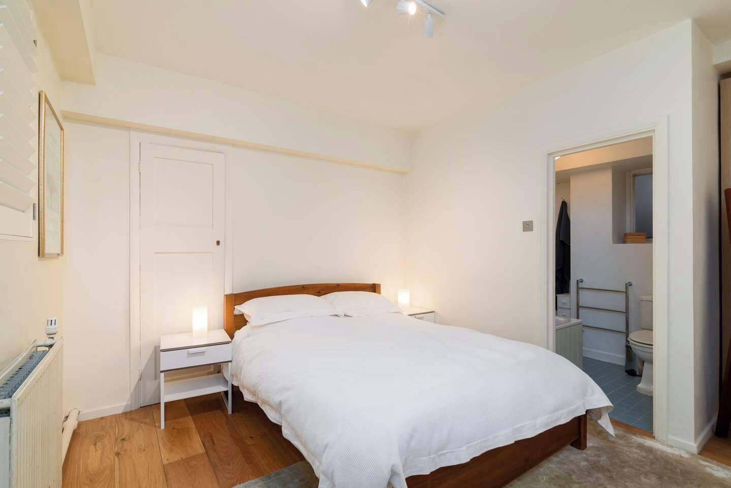 Un dormitorio con cama de madera, ropa de cama blanca, una mesita de noche y una lámpara de noche.