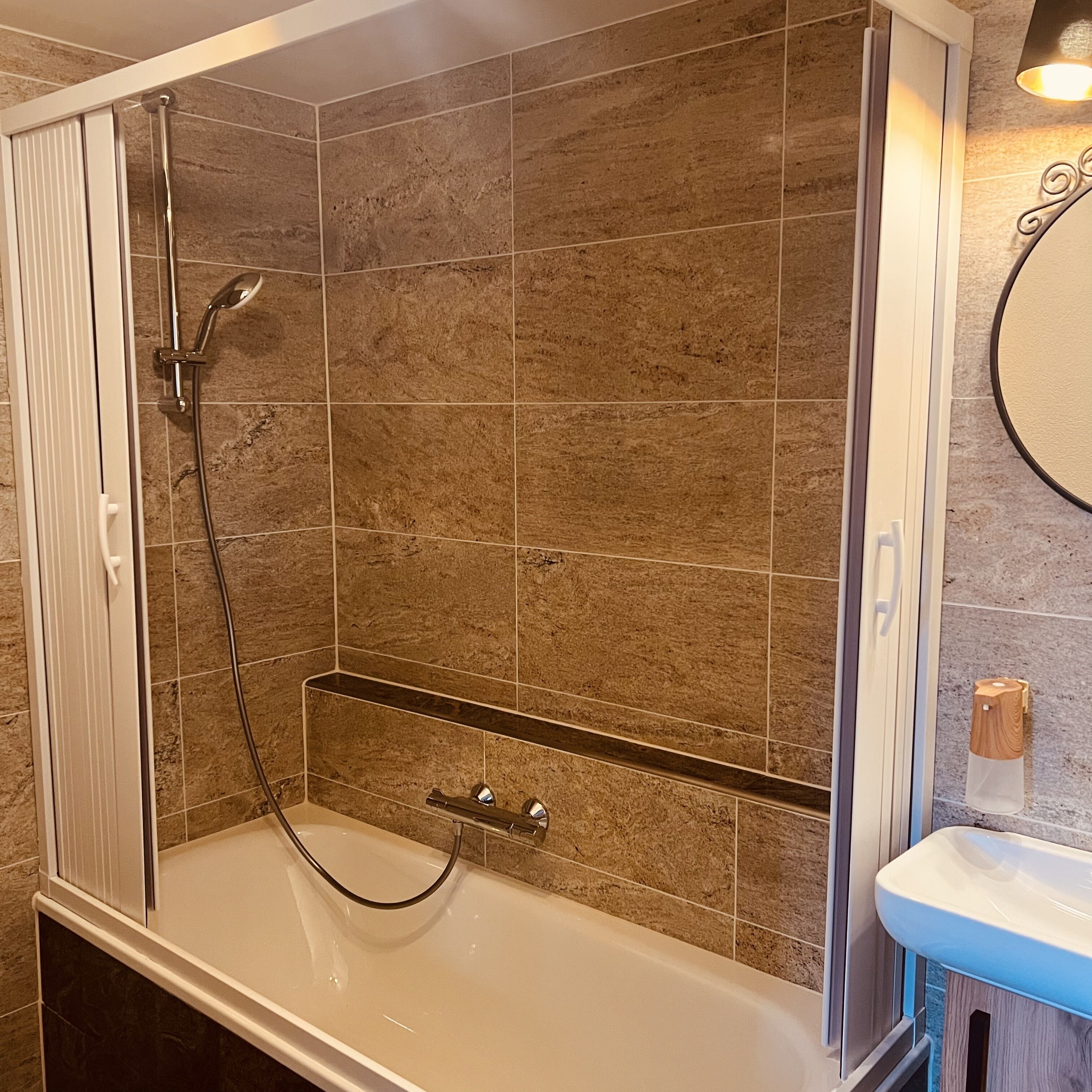 A bathroom with a bathtub, shower, and a vanity with a mirror.