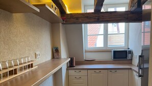 A compact kitchen with white cabinets, a wooden countertop, a window with blinds, and a microwave. - Rose Boardinghouse (Grossbottwar)