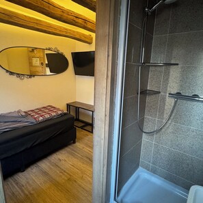 A room with a bed, a small table, a mirror, and a shower area. - Rose Boardinghouse (Grossbottwar)