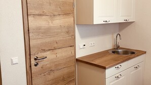 A small kitchenette with a wooden door, white cabinets, a stainless steel sink, and a wooden countertop. - Rose Boardinghouse (Grossbottwar)