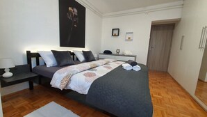 A modern bedroom with a large bed, a bedside table, a nightstand, a wardrobe, and a door. - Apartment Pallaton (Nasice)