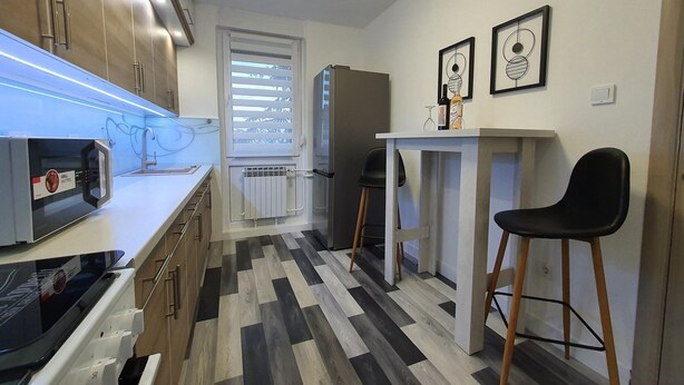 A modern kitchen with a microwave, a refrigerator, and a dining area with a chair and table. - Apartment Pallaton (Nasice)
