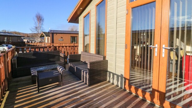 Een houten terras met rieten meubilair en een glazen deur naar een overdekt gedeelte.