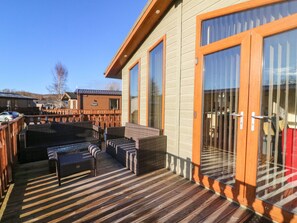 Una terraza de madera con mobiliario de mimbre y un ventanal que da a un espacio cubierto.