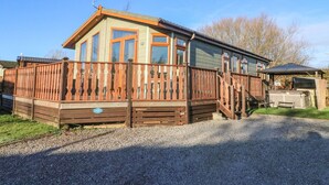 Een houten chalet met een terras, grote ramen en een grindpad.