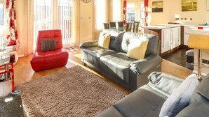 Een moderne woonkamer met een rode fauteuil, een grijze bank en een eethoek met een glazen tafel.