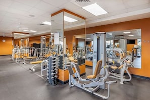 A gym with various exercise machines, mirrors, and a clock on the wall.