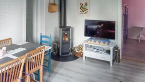 Een gezellige woonkamer met een open haard, een televisie en een eethoek met stoelen en een tafel.