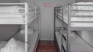 Een smalle gang met stapelbedden aan weerszijden, een bord aan de muur en een rood tapijt dat naar de bedden leidt.