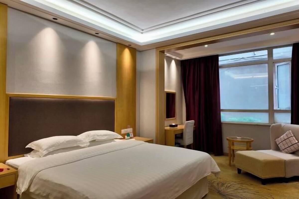 A hotel room with a large bed, a desk, a chair, and a sofa.