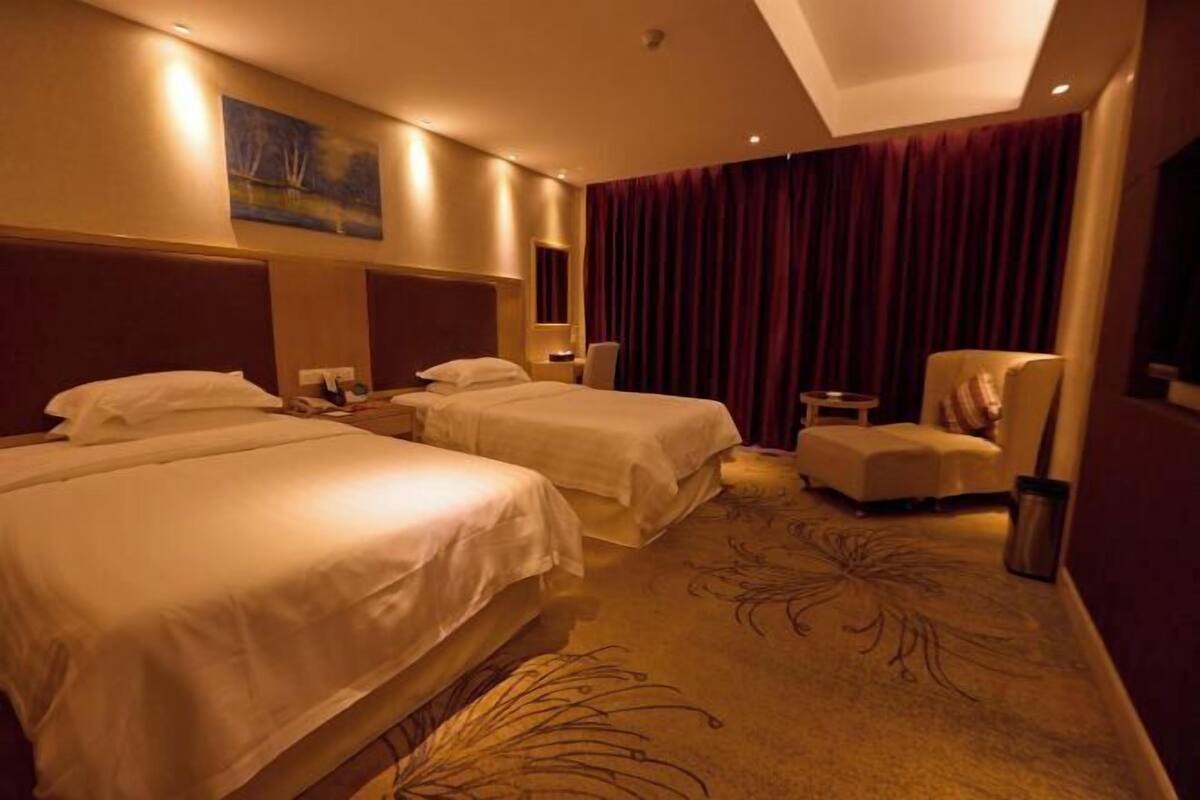 A hotel room with two beds, a small table, a chair, and a painting on the wall.