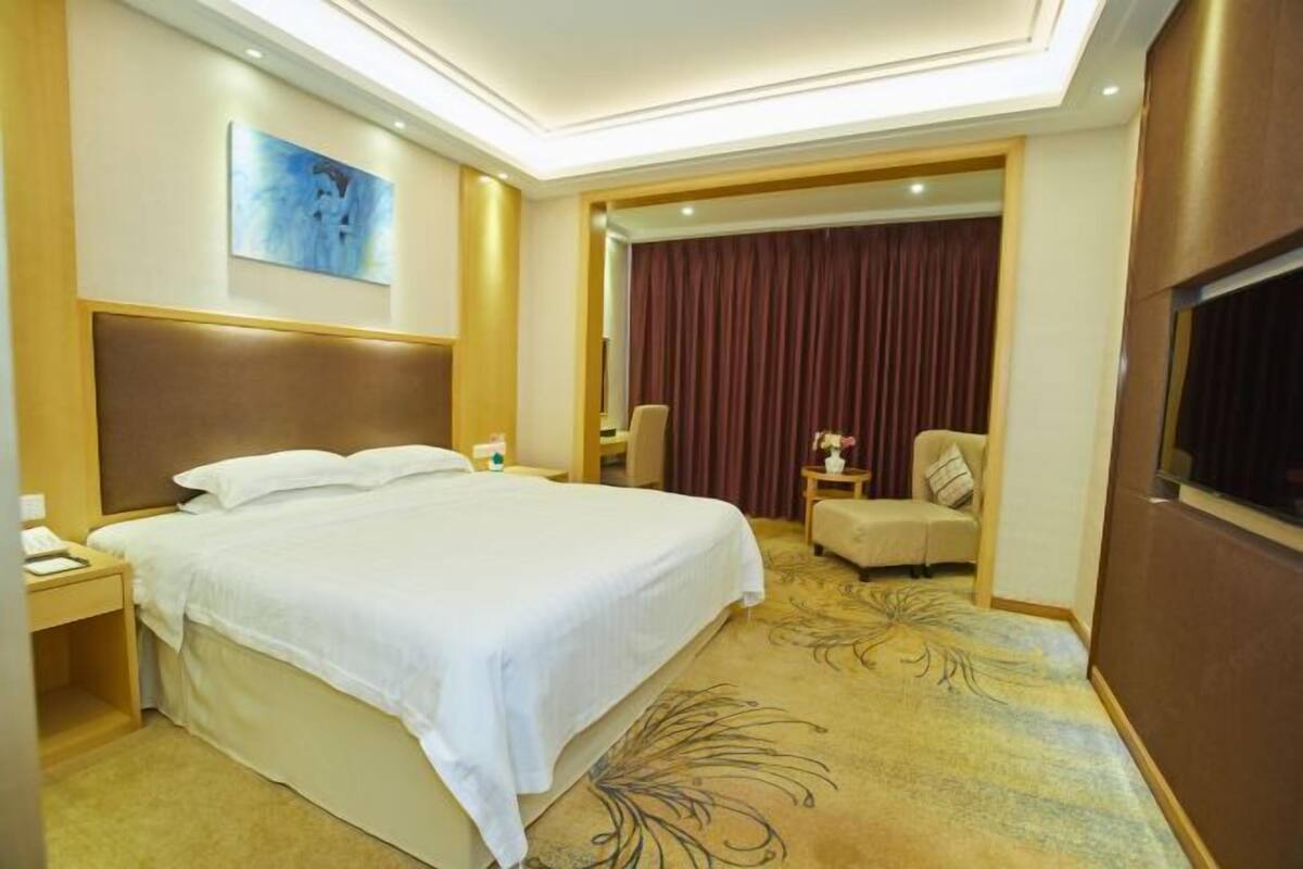 Habitación de hotel con una cama grande, una mesita de noche, una silla, una pequeña mesa con un florero y un televisor en la pared.
