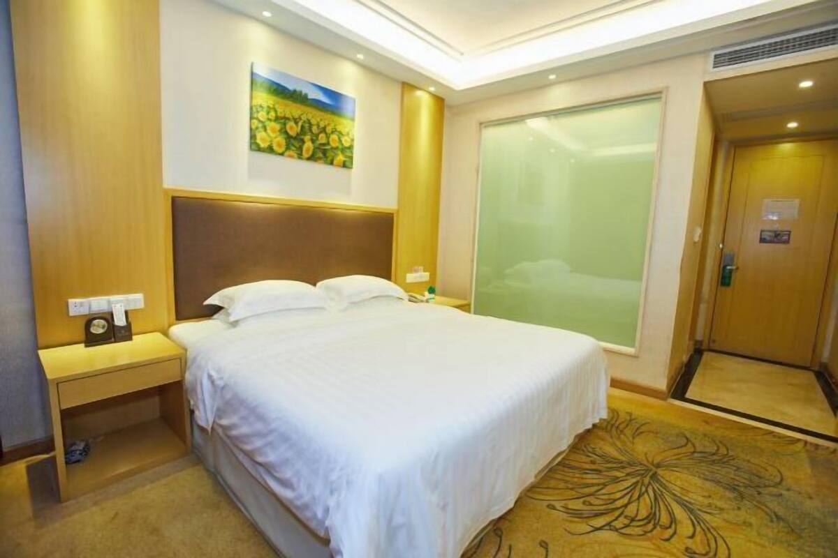 Una habitación de hotel con una cama grande, una mesita de noche con lámpara, un cuadro en la pared y una puerta corredera.