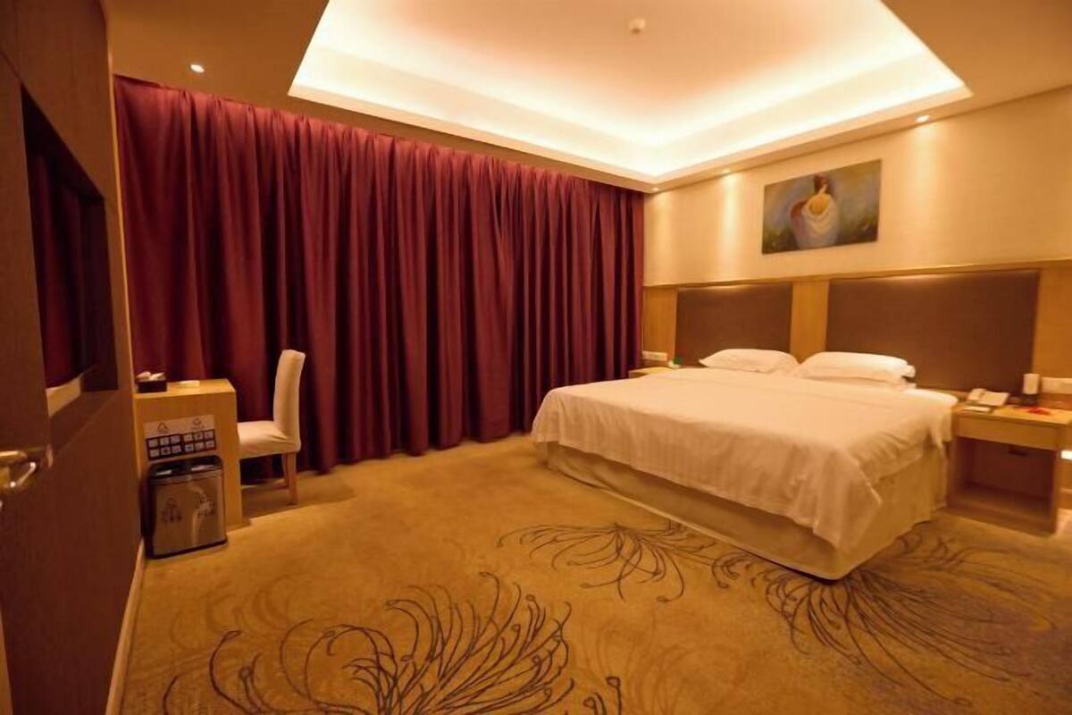 A hotel room with a large bed, a desk with a chair, a nightstand, and a painting on the wall.