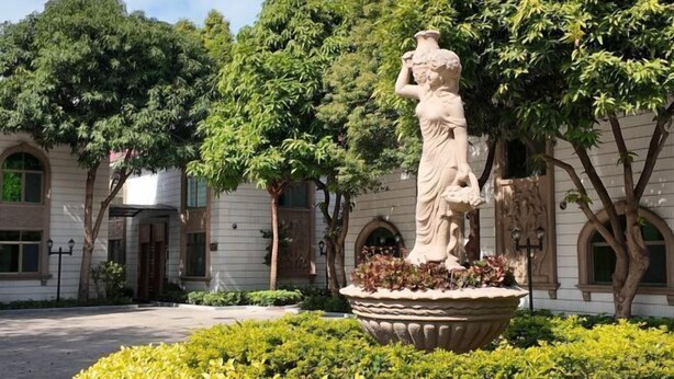 Un patio con una estatua, abundante vegetación y un edificio con ventanas arqueadas.