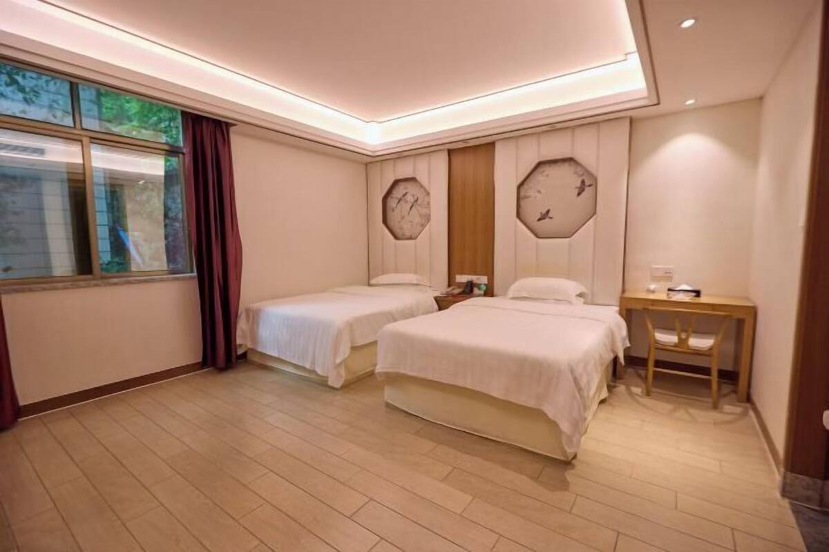 A hotel room with two beds, a wooden desk, and a large window with curtains.
