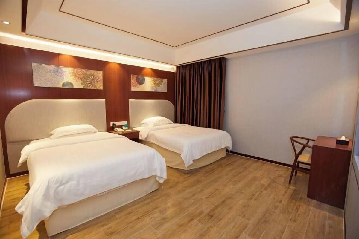 A hotel room with two beds, wooden flooring, a desk, and artwork on the walls.
