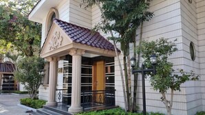 Un edificio de estilo arquitectónico clásico, que destaca por su entrada con tejado de azulejos, columnas y puerta de madera.