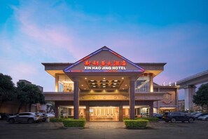 The entrance of Xin Hao Jing Hotel with a prominent sign, a covered entrance area, and a parking lot with cars. - New Haojing Hotel (Guangzhou Xintang Metro Station) (Guangzhou)