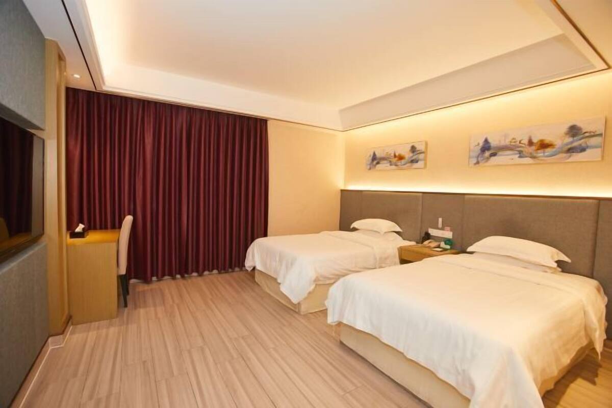 A hotel room with two beds, a desk, and a window with curtains.
