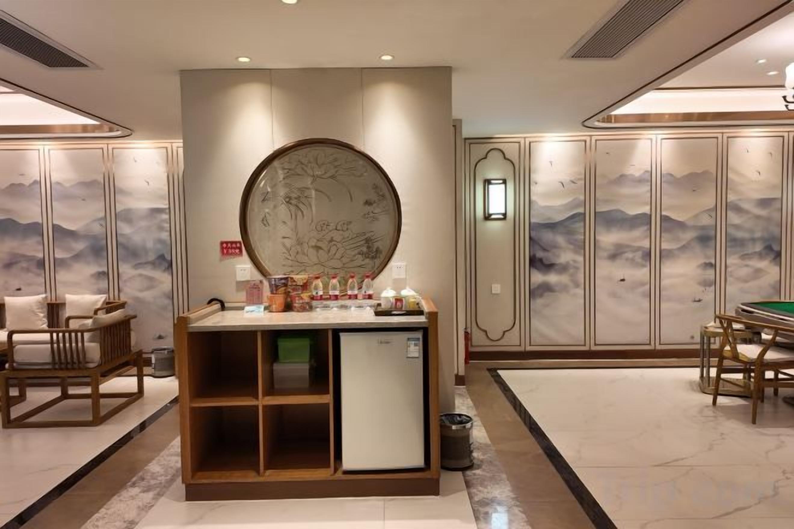 A hotel room with a traditional design, featuring a wooden cabinet, a small refrigerator, and a dining area with a table and chairs.