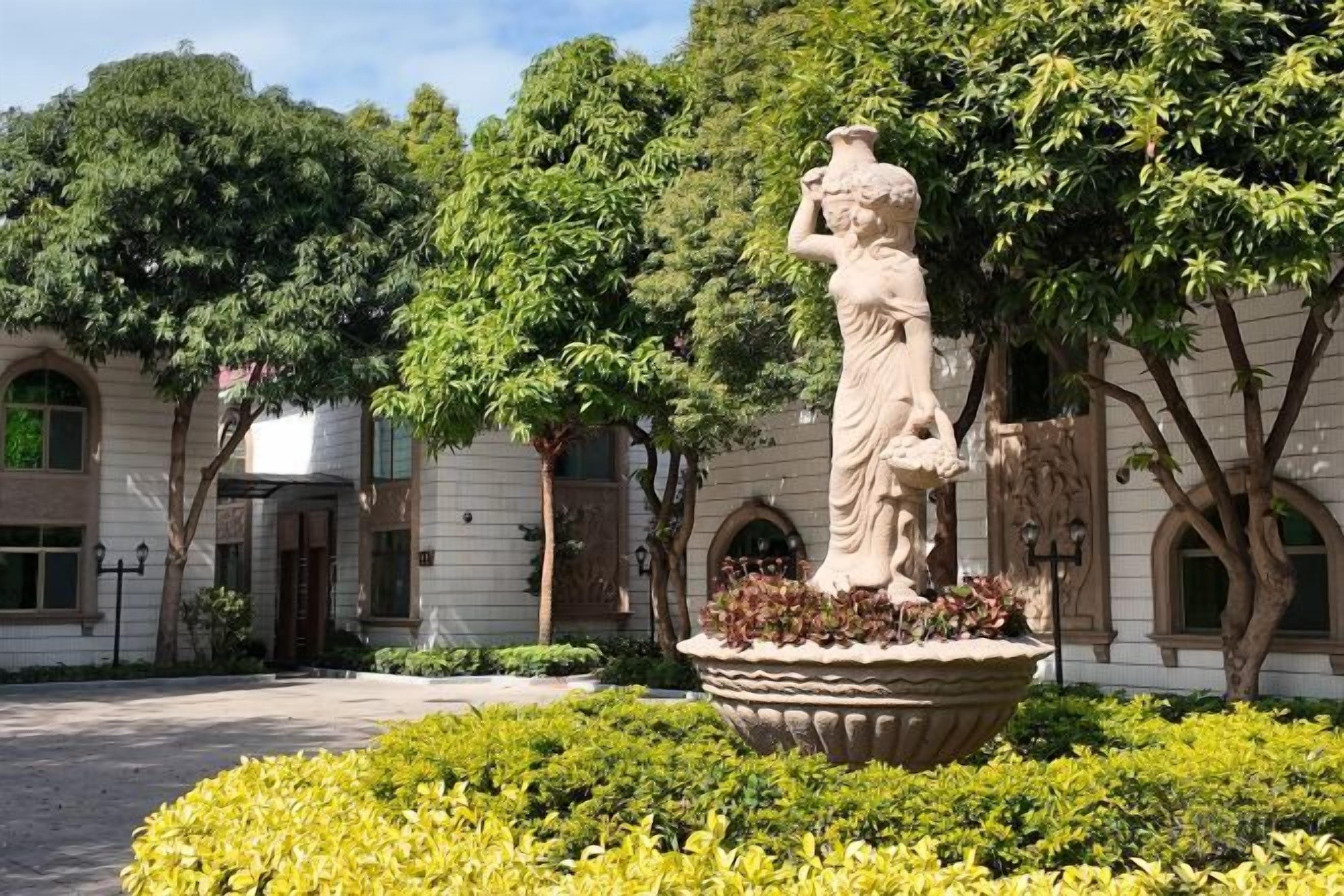 A courtyard with a statue, trees, and a building with arched windows.
