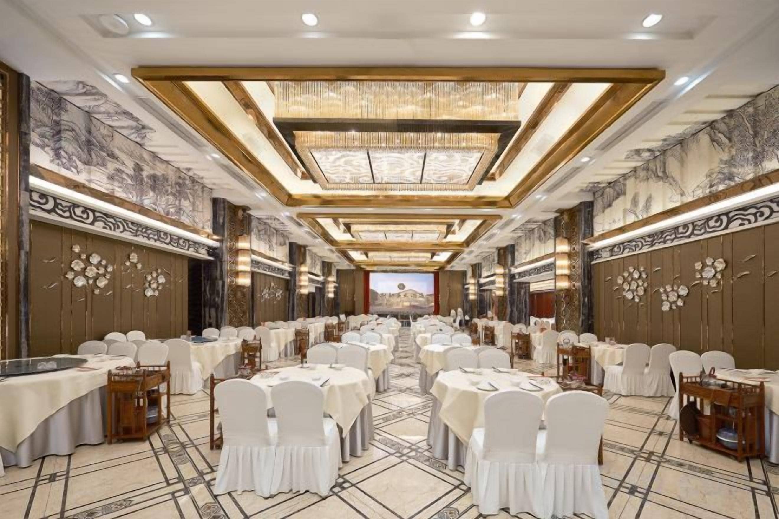 Un salón de banquetes con mesas redondas, sillas blancas y un pasillo central.