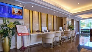 Zona de recepción de un hotel con una pantalla digital mostrando información de habitaciones, un mostrador de recepción y un área de estar con taburetes de bar.