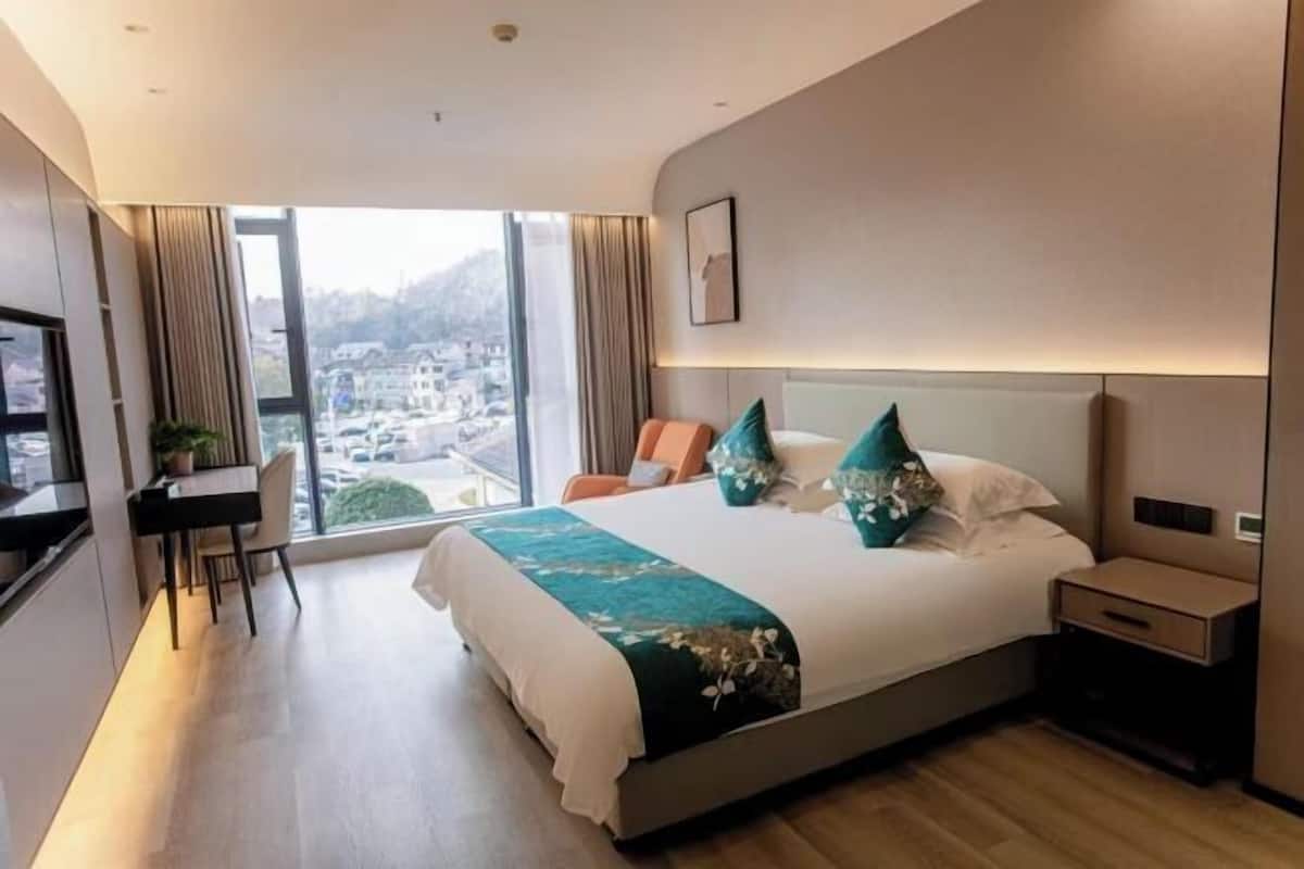 Habitación de hotel moderna con una cama grande, un escritorio y vistas a un paisaje urbano.