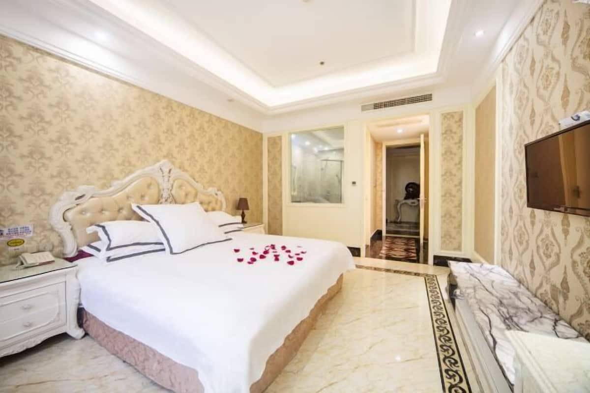 Habitación de hotel con una cama grande, una mesita de noche, un televisor y un baño visible a través de una puerta abierta.