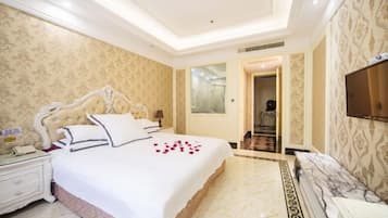 Quarto de hotel com uma cama grande, mesa de cabeceira, televisão e banheiro visível através de uma porta aberta.