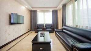 Un salon doté d’un téléviseur à écran plat fixé au mur, d’un canapé en cuir noir, de deux fauteuils, d’une table basse et d’une grande fenêtre avec des rideaux.