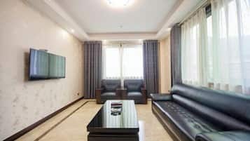 Una sala de estar con una televisión de pantalla plana montada en la pared, un sofá de cuero negro, dos sillones, una mesa de centro y un ventanal con cortinas.