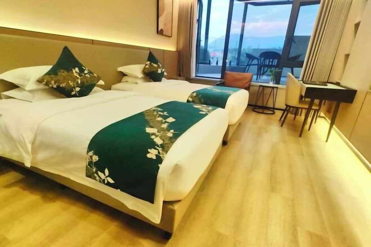 Habitación de hotel con dos camas, un escritorio y vistas al exterior.