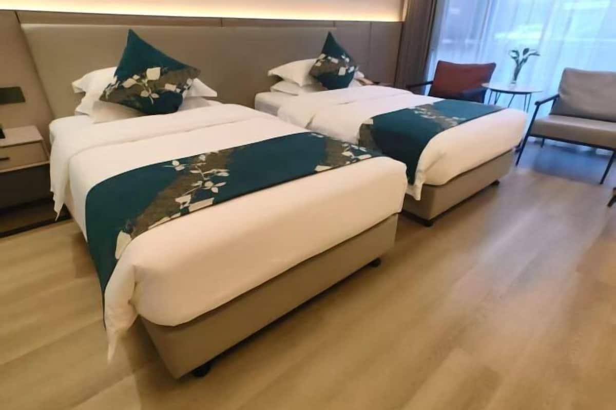 Habitación de hotel con dos camas, una mesita, una silla y vistas al exterior.