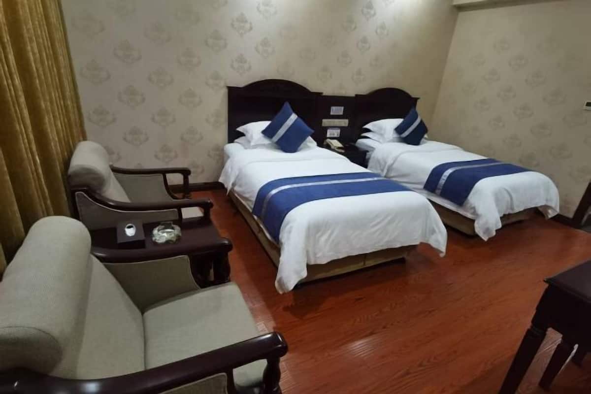 Una habitación de hotel con dos camas, un sofá, una mesita y suelo de madera.