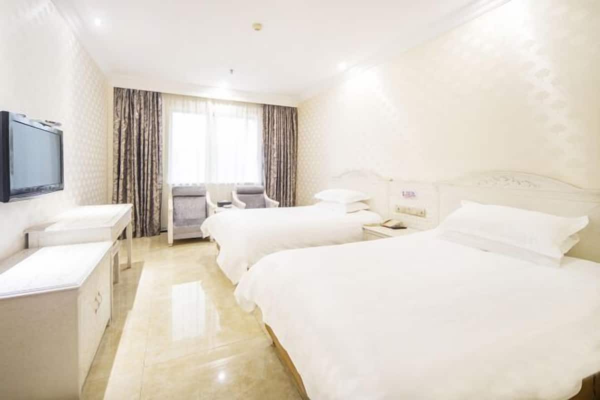 Habitación de hotel con dos camas, un escritorio, una silla, un televisor y una ventana con cortinas.