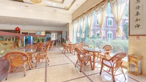 Un hall d’hôtel avec des meubles en osier, de grandes fenêtres et un lustre.