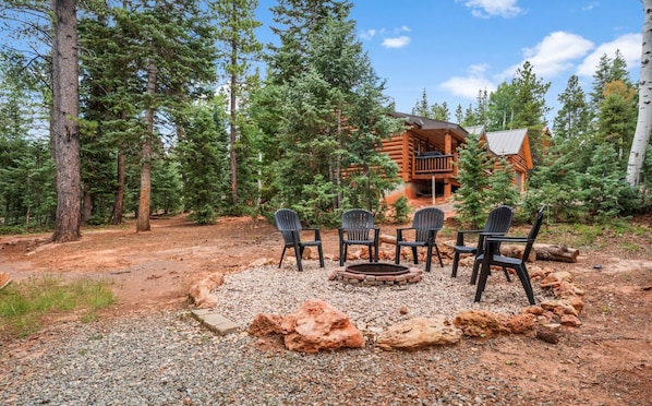 A cabin with a fire pit and four chairs in a forested area.