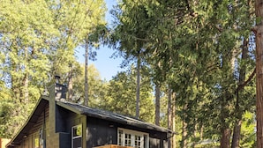 Eine Holzhütte mit einer Wendeltreppe, die zu einer Terrasse führt, umgeben von hohen Bäumen.