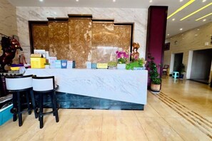 A reception desk with a marble top, black chairs, and a potted plant. - Xiongfeng Hotel (Nanhua)