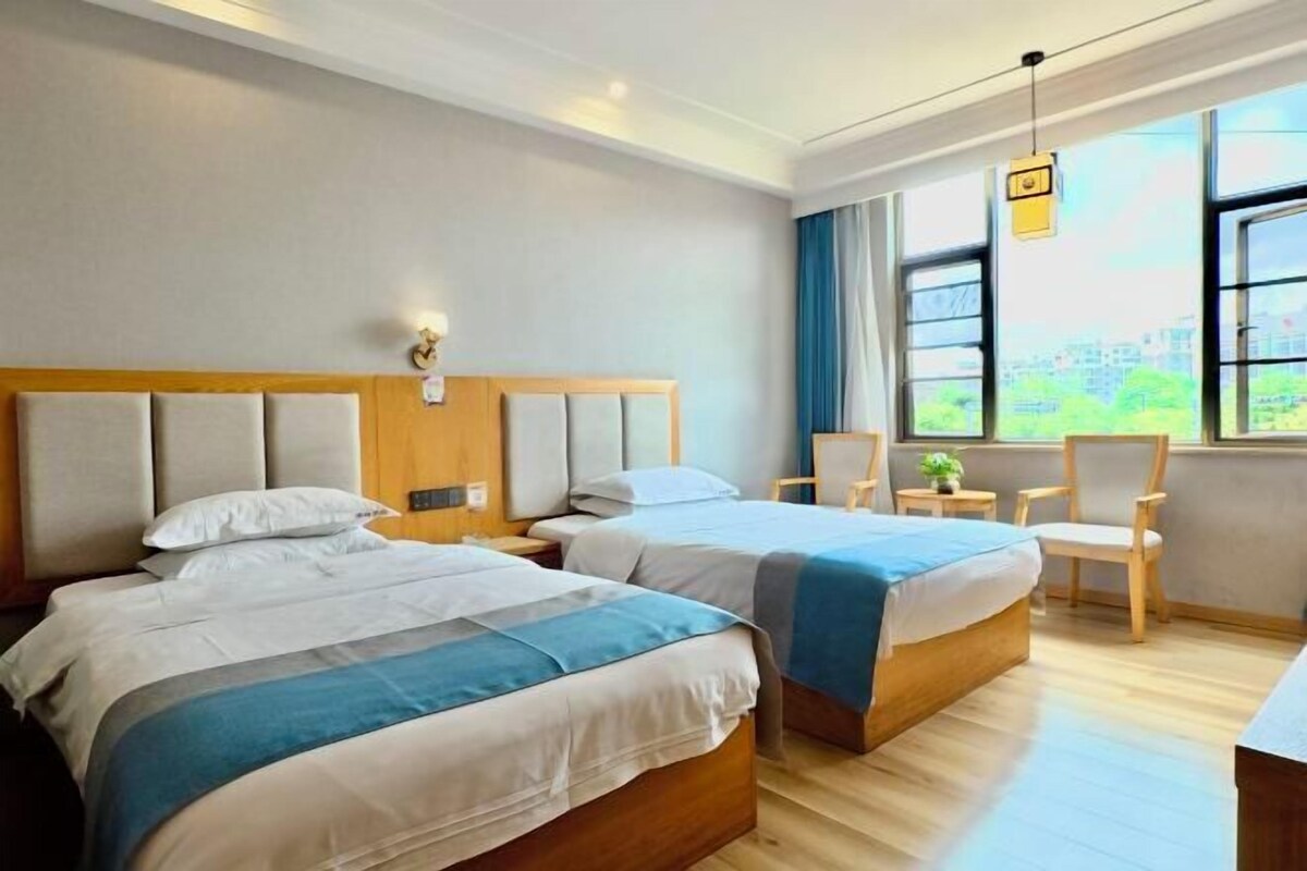 Ein Hotelzimmer mit zwei Betten, Blick auf die Stadt, Holzboden und einem Sessel am Fenster.