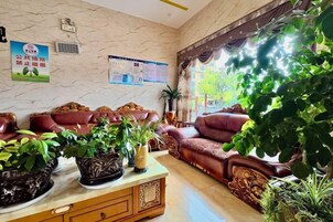 A reception area with a marble wall, red sofas, a wooden cabinet with potted plants, and a window with a view of greenery.