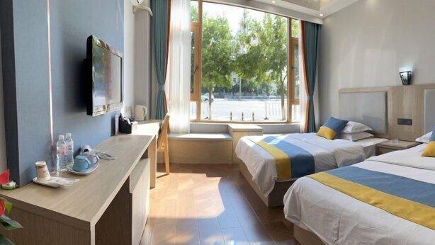 A hotel room with a desk, two beds, a TV, and a window with a view of the street.