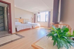 Quarto de hotel com duas camas, piso de madeira, uma janela grande e um vaso com planta.