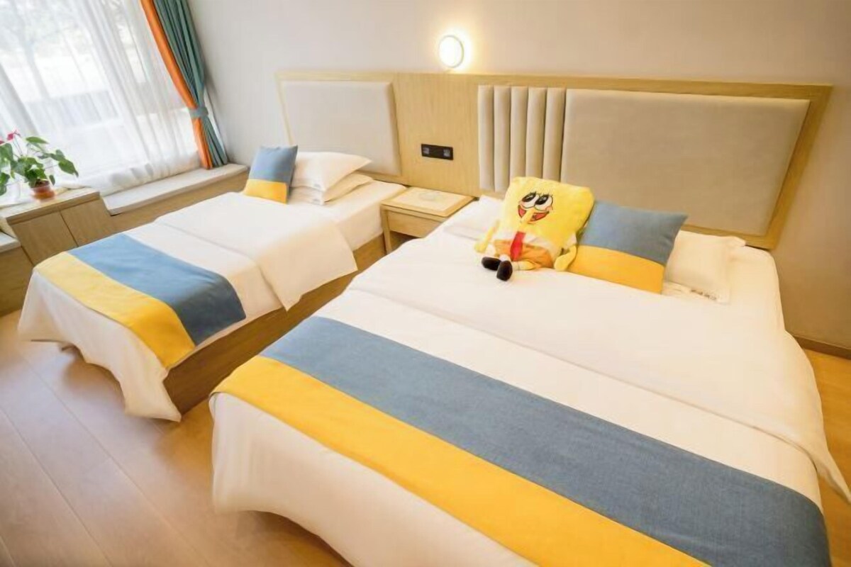 Ein Hotelzimmer mit zwei Betten, einem Nachttisch, einer Lampe und einem Fenster mit Vorhängen.