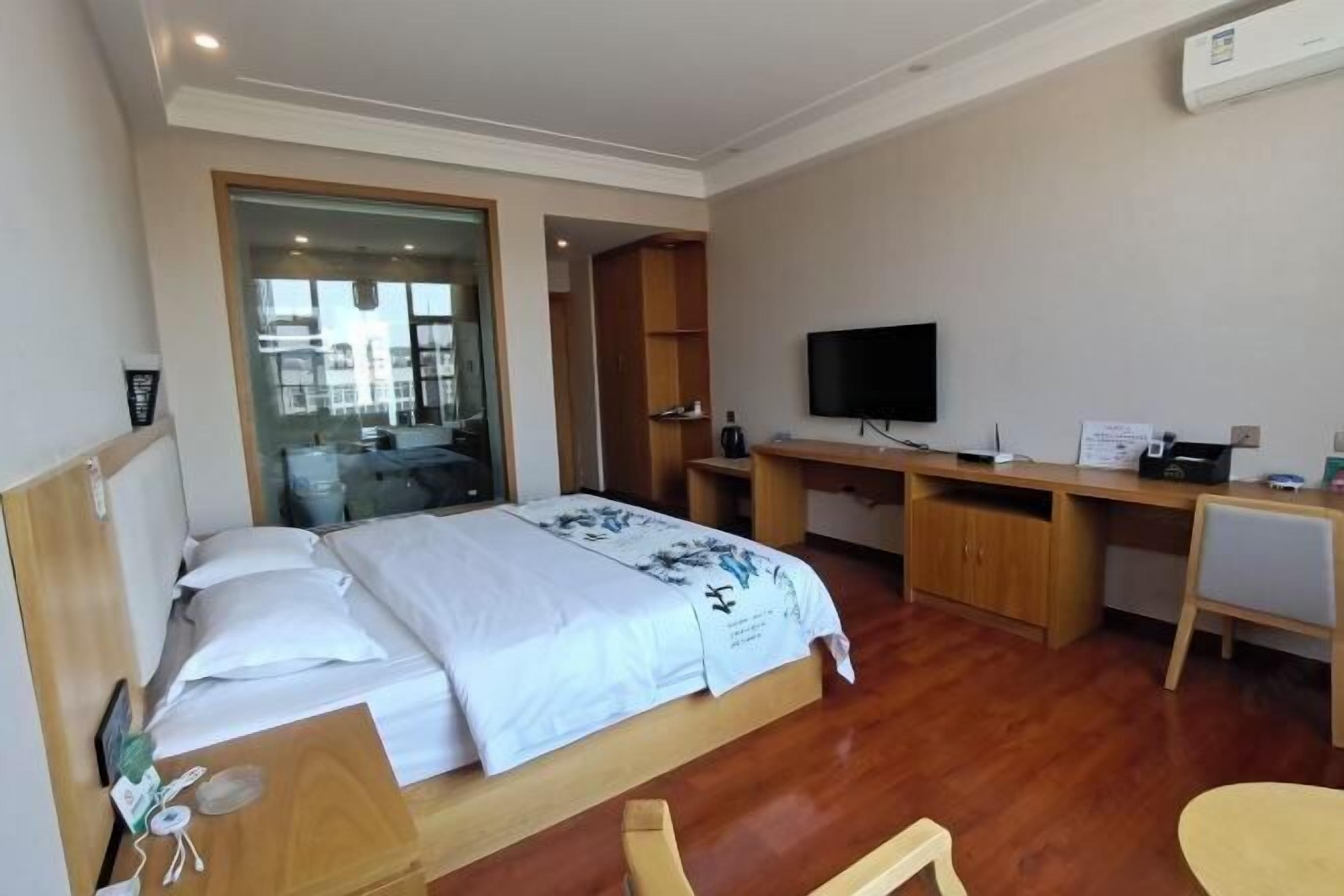 Une chambre d’hôtel avec un lit, un bureau, une télévision et une vue sur l’extérieur, visible à travers une porte vitrée.