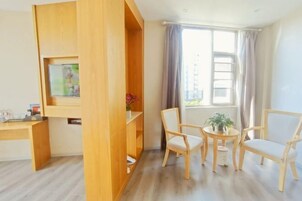 A room with a wooden desk, two chairs, a small table with a plant, and a window with curtains.